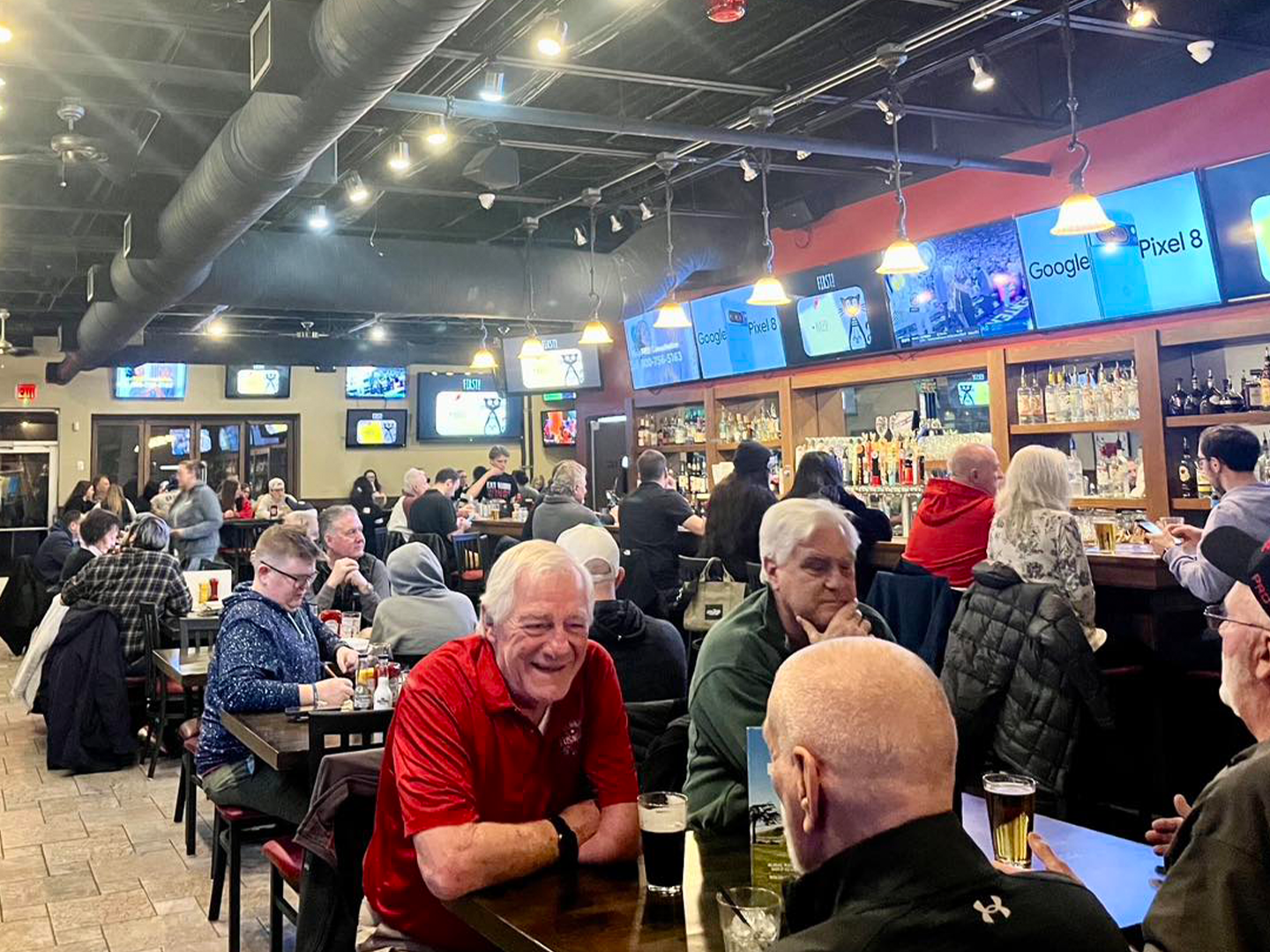 Lively crowd enjoying food and drinks at McWethy’s Sports Bar, with wall-to-wall TVs and a full-service bar.