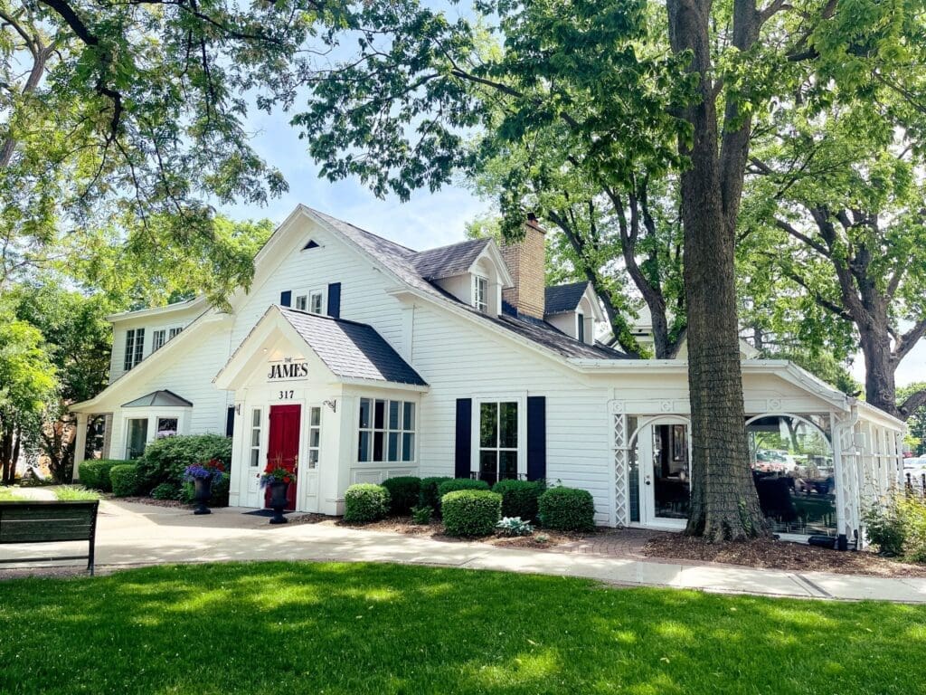 The James restaurant, a white historic house with a red door, surrounded by lush greenery.