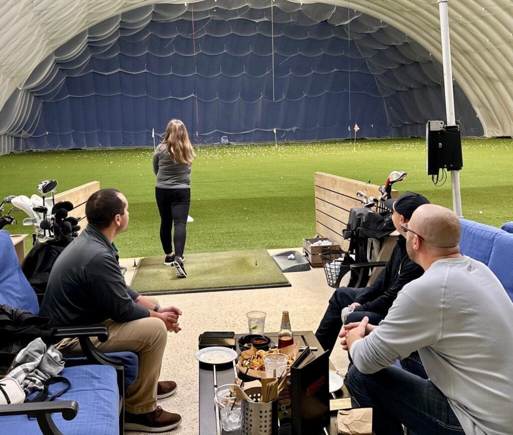 Guests enjoying a virtual golf experience at Mistwood Golf Dome with food and drinks at the bay.