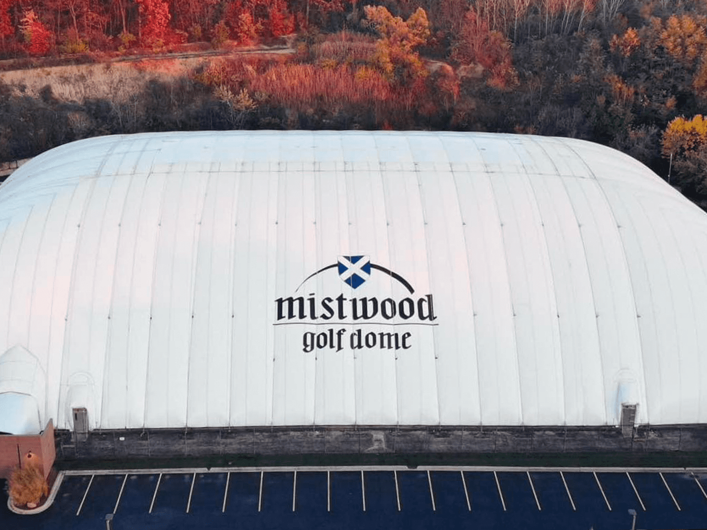 Aerial view of Mistwood Golf Dome with logo and surrounding autumn foliage.