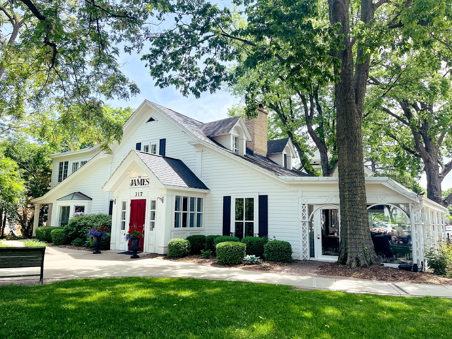 Exterior of The James Restaurant in Geneva, Illinois, a charming white historic home with red front door and lush landscaping.