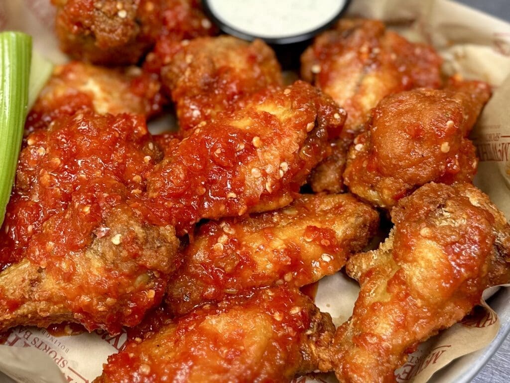 Plate of THE FARM FERMENTED HOT HONEY JUMBO WINGS from McWethy’s Sports Bar with celery and dipping sauce.